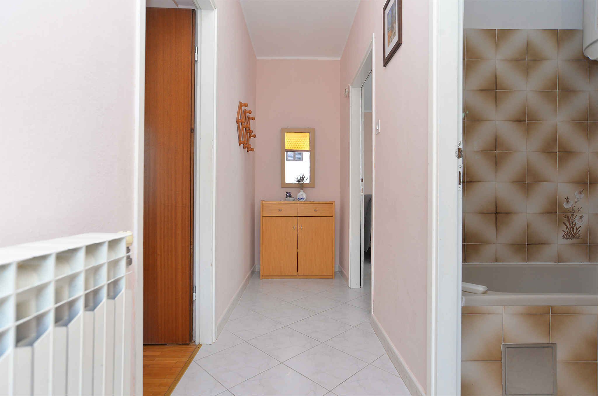 A narrow hallway with a wooden door, a small cabinet, and a tiled floor.