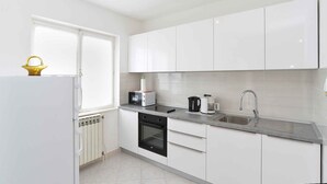 A modern kitchen with white cabinets, a built-in oven, a sink, and a window. - Holiday apartment with air conditioning (Rabac)