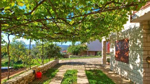 A paved pathway leading to a building with a stone wall and a red bucket on the left. - Holiday apartment with air conditioning (Rabac)