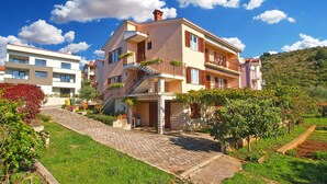 A multi-story building with a stone staircase leading to the entrance, surrounded by lush greenery and a vineyard. - Holiday apartment with air conditioning (Rabac)