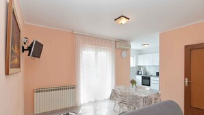 A living room with a sofa, a small table, a TV mounted on the wall, a dining area with a table and chairs, and a kitchen in the background. - Holiday apartment with air conditioning (Rabac)
