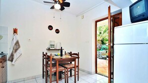 A compact kitchen with a dining area, a ceiling fan, a refrigerator, and a view of the outdoors through a door.