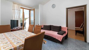 A room with a dining table, chairs, a sofa, a television, and a clock on the wall.