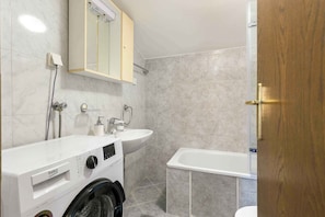 Une salle de bain équipée d’un lave-linge, d’un lavabo et d’une baignoire.