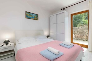 Camera da letto con un letto, un comodino, una lampada, un quadro e una porta scorrevole verso uno spazio esterno.