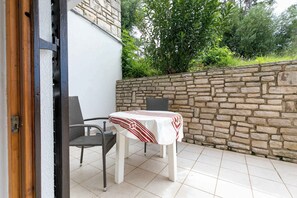 Une terrasse extérieure avec une table et des chaises, un mur en pierre et une porte donnant sur un espace intérieur.