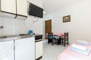 Eine kleine Küche mit Fernseher, einem Esstisch mit Stühlen und einem Bett mit Handtüchern.
