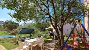 An outdoor patio with a table and chairs, a barbecue grill, a swing set, and a pool. - Holiday apartment with air conditioning (Štinjan)