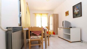 A small, well-lit room with a wooden table and chairs, a radiator, a white cabinet with a television, and a window with curtains. - Holiday apartment with air conditioning (Štinjan)
