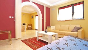A room with a bed, a sofa, a dining table, and a red rug.