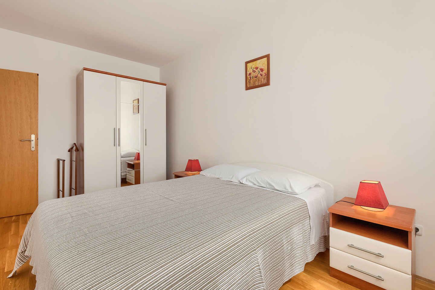 Een slaapkamer met een bed, een kledingkast, een nachtkastje en een kleine tafel met lamp.