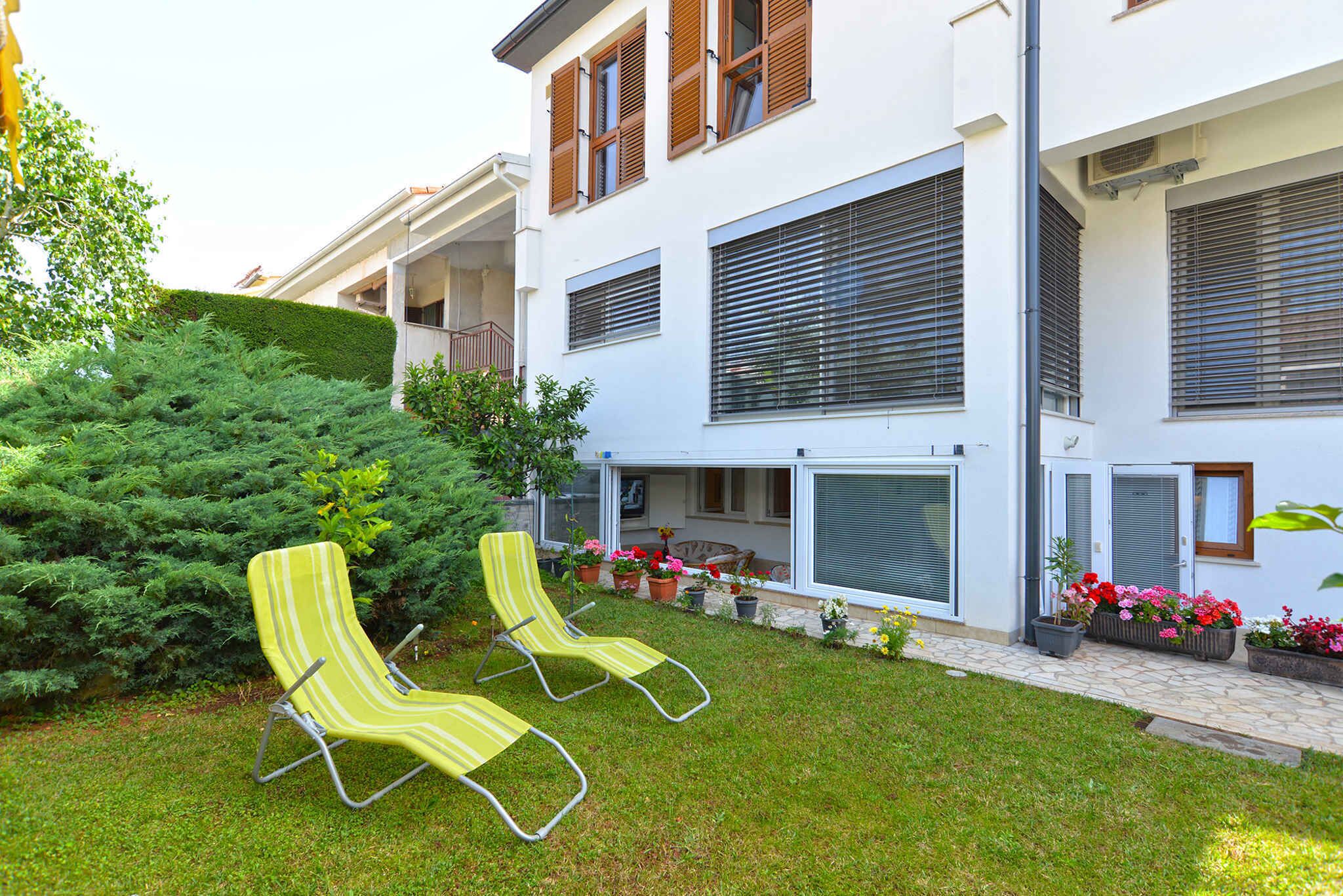 A modern two-story building with a balcony, a well-maintained lawn, and two striped lounge chairs.