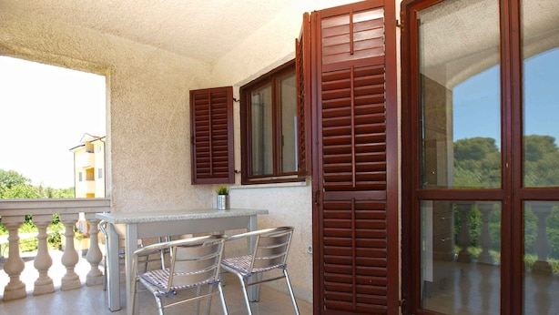 An outdoor balcony with a table and chairs, wooden shutters, and a view of greenery. - Holiday apartment with balcony (Valbandon)