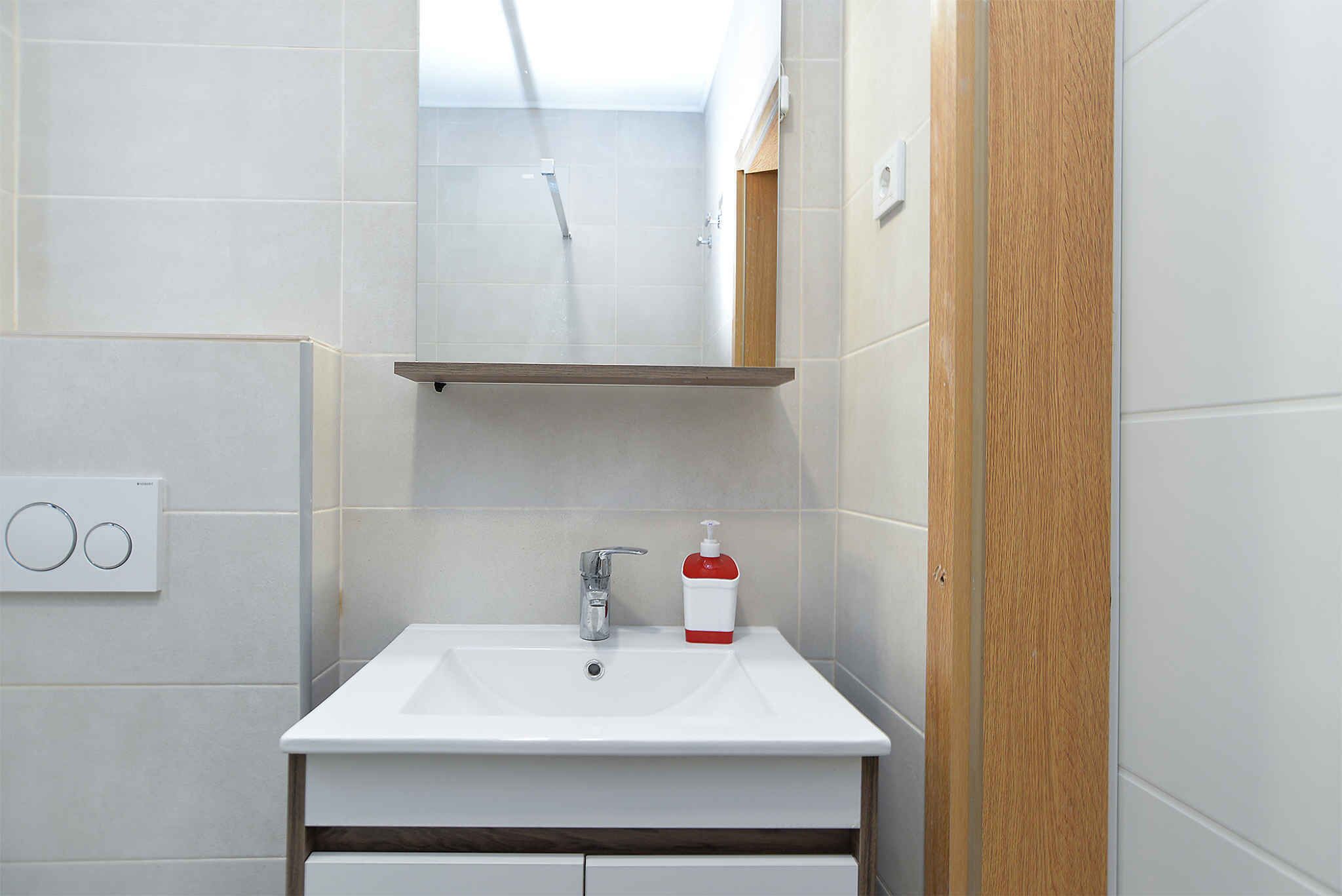 Un bagno con un lavandino bianco, uno specchio e una porta in legno.