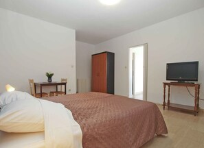 Ein Schlafzimmer mit einem Bett, einem Schreibtisch mit Fernseher, einem Heizkörper und einem Kleiderschrank.