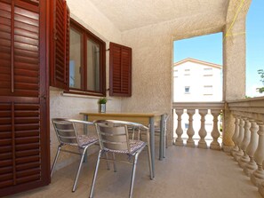 Ein Balkon mit zwei Metallstühlen, einem Holztisch und einem Fenster mit Holzklappläden.