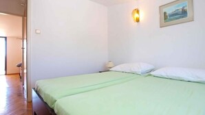 A room with two beds, a wooden floor, a painting on the wall, and a nightstand with a lamp. - Holiday apartment with air conditioning (Štinjan)