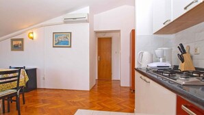 A kitchen with a stove, a coffee maker, and a knife block. There is a dining area with a table and chairs. - Holiday apartment with air conditioning (Štinjan)