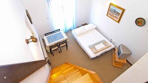 Une chambre à coucher avec un lit, un bureau et une chaise. Il y a une fenêtre avec des rideaux, un tableau au mur et un escalier menant à un autre étage.