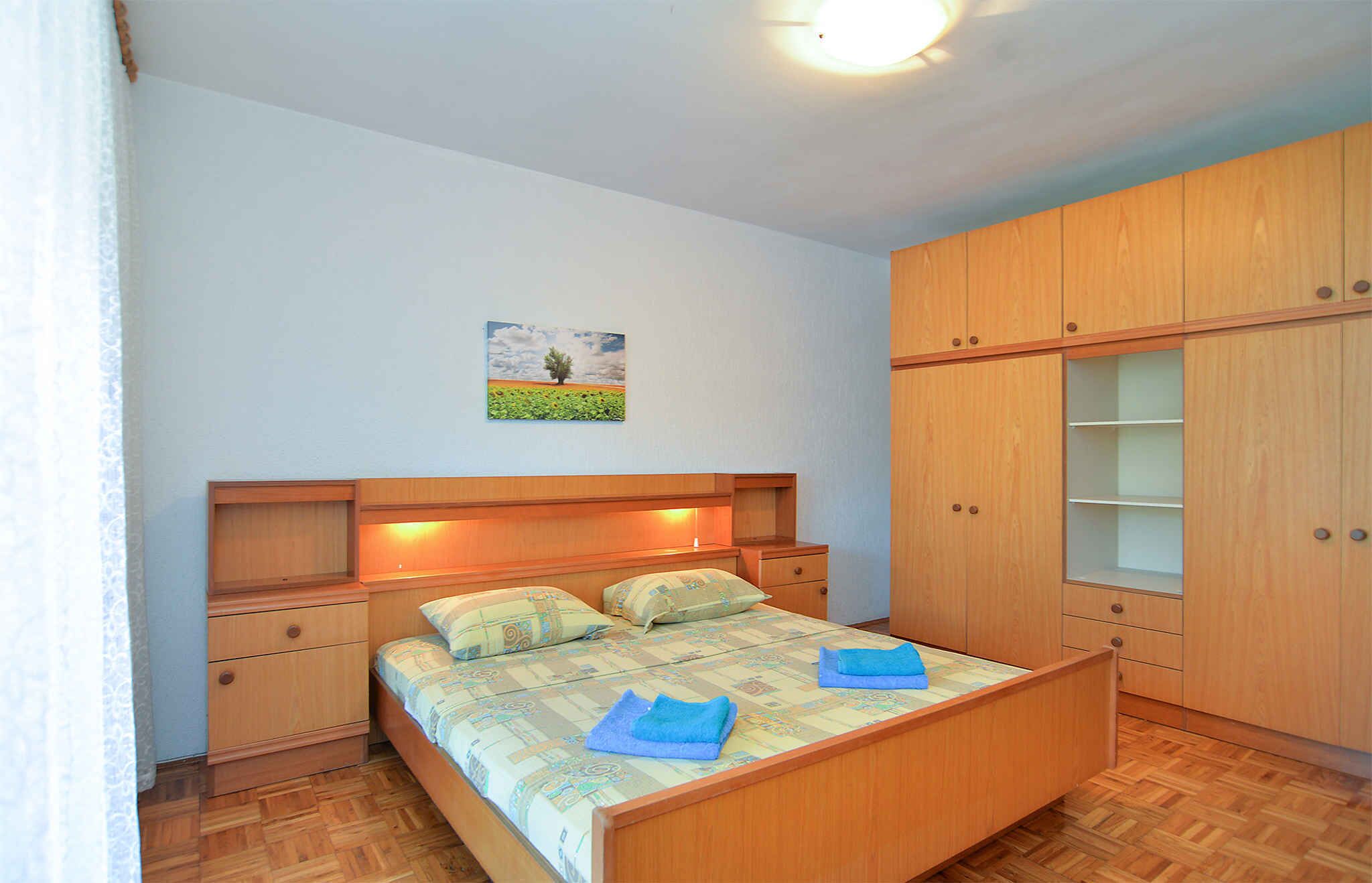 A bedroom with a bed, wooden wardrobe, and a painting on the wall.