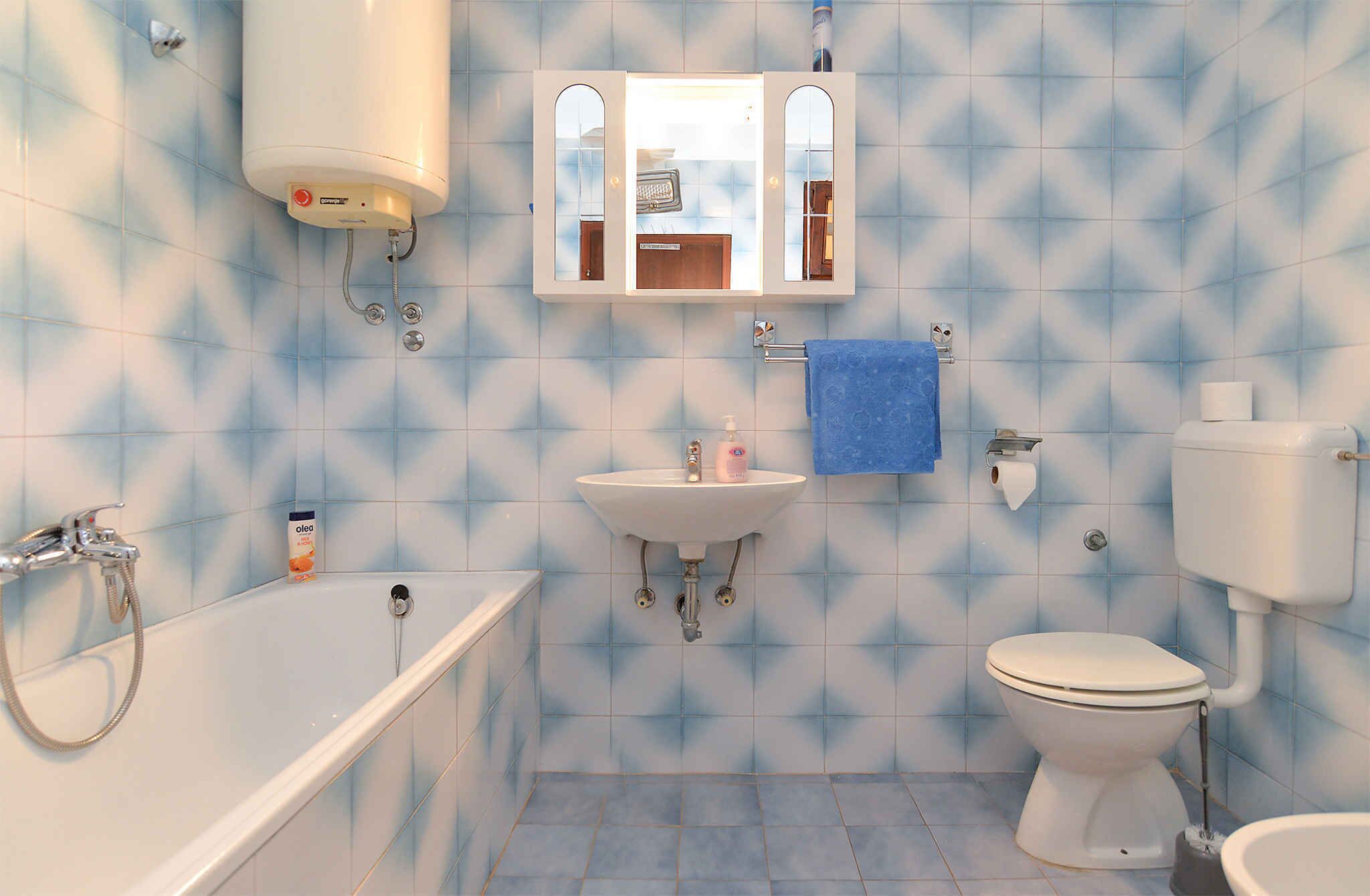 Een badkamer met een bad, wastafel, toilet en een spiegel boven de wastafel.