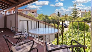 Een balkon met een ronde tafel en twee stoelen, een uitzicht op omliggende huizen en een heldere lucht.