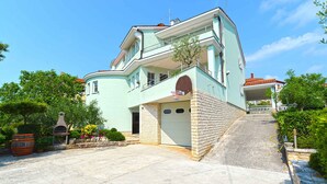 A two-story house with a garage, a brick facade, and a small garden with potted plants and a barbecue grill. - Holiday apartment with air conditioning (Pula)