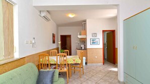 A compact living space with a green sofa, wooden dining table with chairs, a kitchenette, and a green wardrobe. - Holiday apartment with air conditioning (Pula)