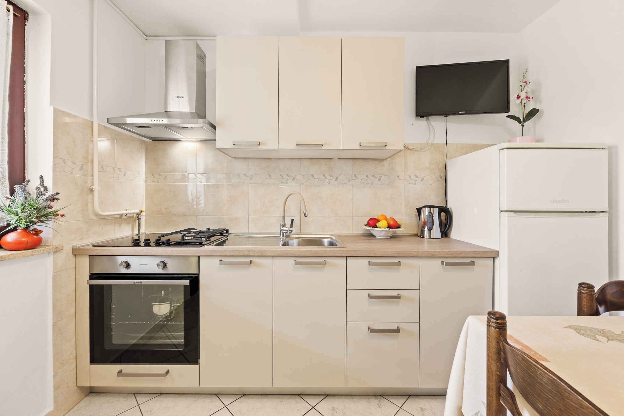 A compact kitchen with a built-in oven, a gas stove, a stainless steel range hood, a sink, and a small refrigerator.