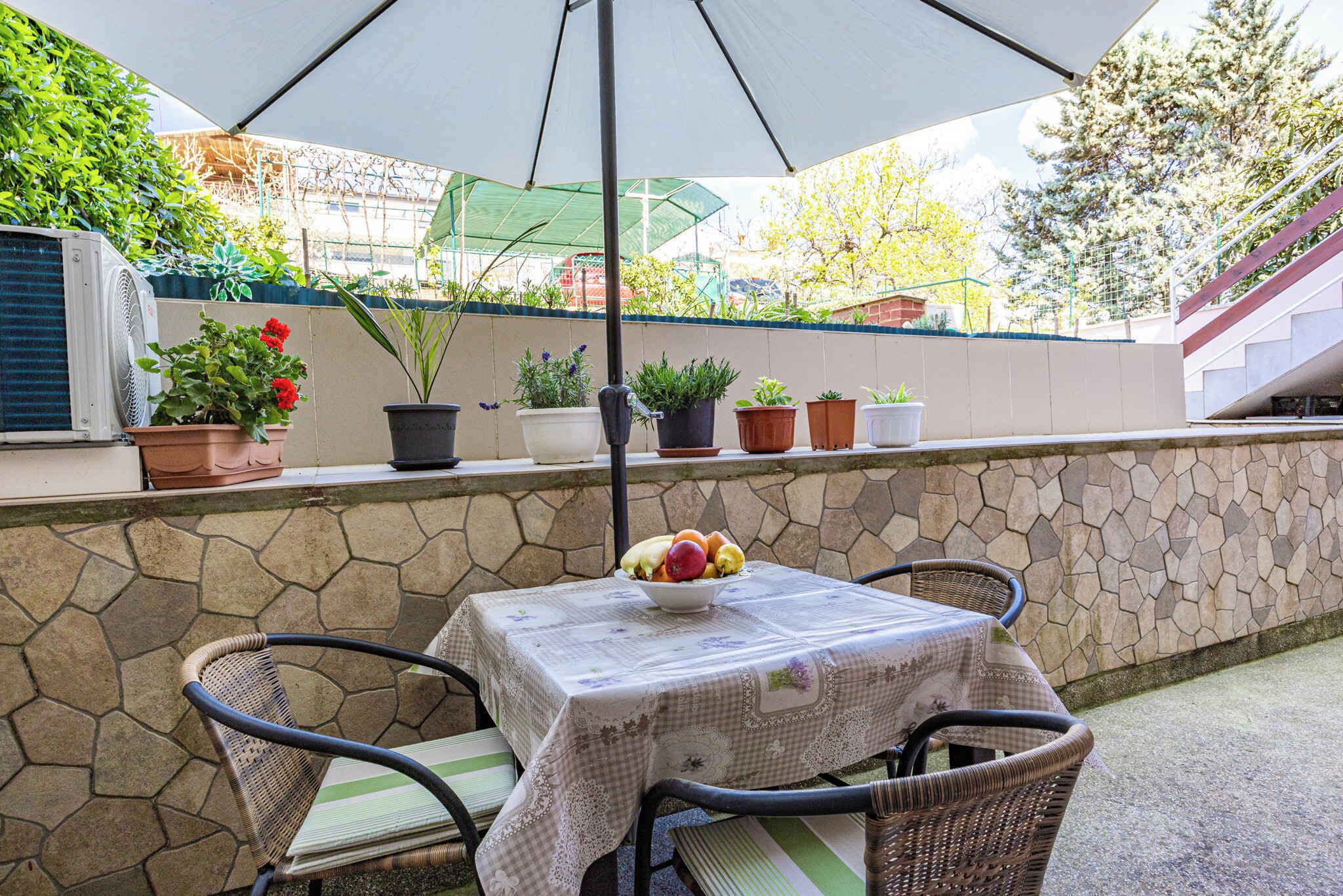 En terrasse med et bord og stole, omgivet af plantekrukker og en stenvæg.
