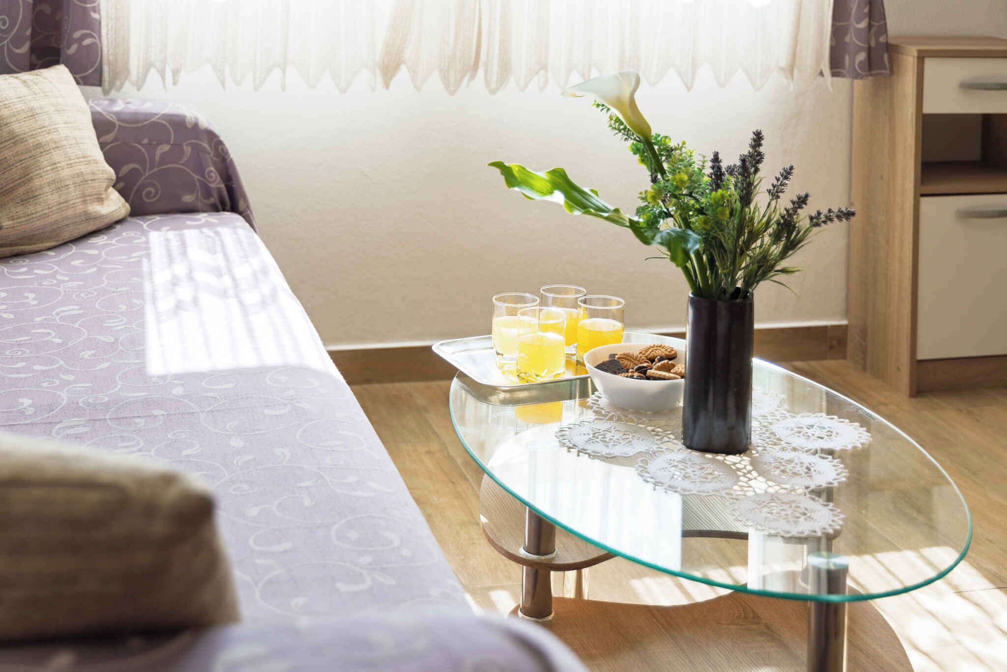 A glass-top table with a vase of flowers, a bowl of cookies, and glasses of orange juice.