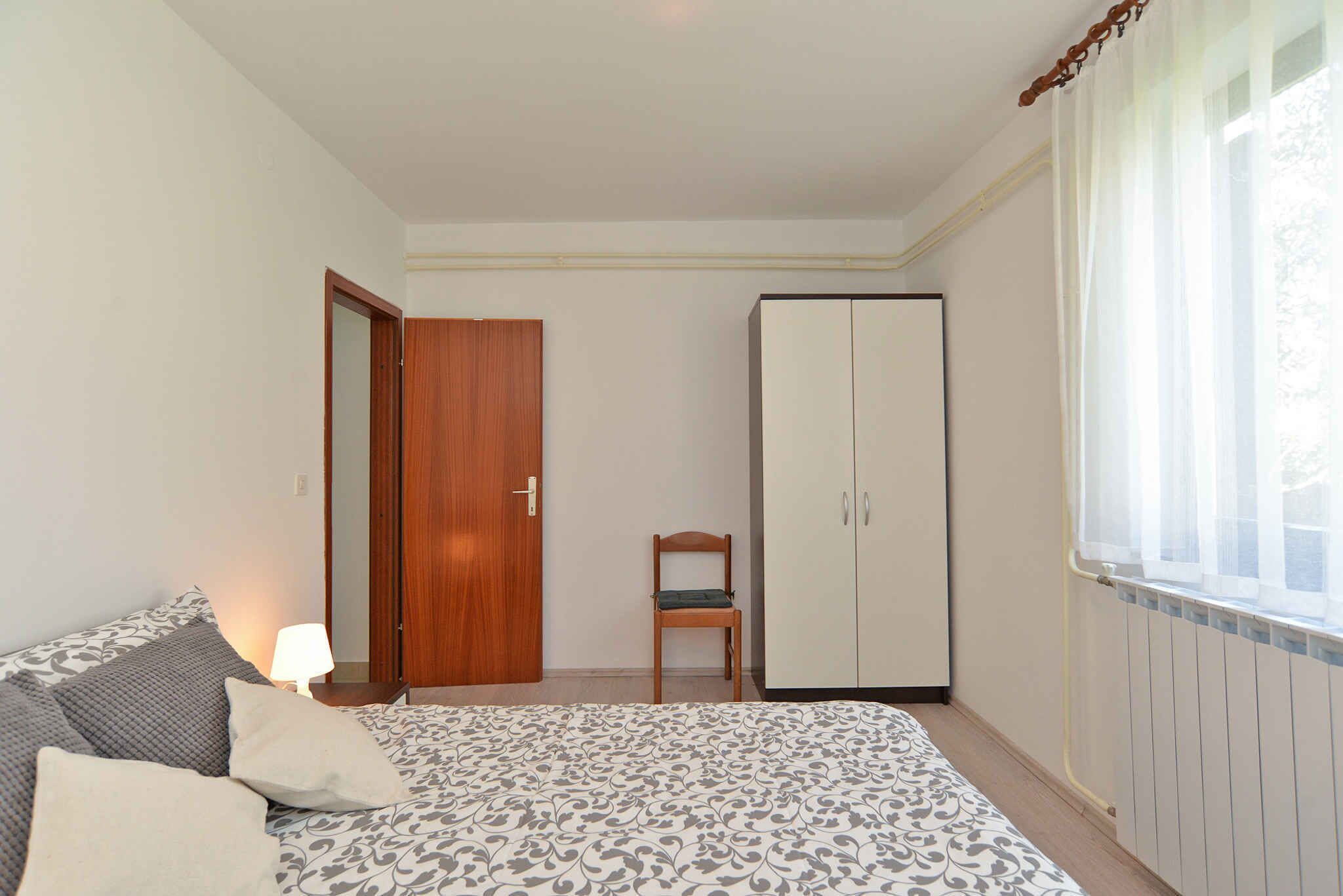 Une chambre à coucher avec un lit, une porte en bois, une armoire, une chaise et une fenêtre avec des rideaux.