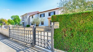 A two-story house with a gated driveway, a well-maintained hedge, and a clear blue sky.