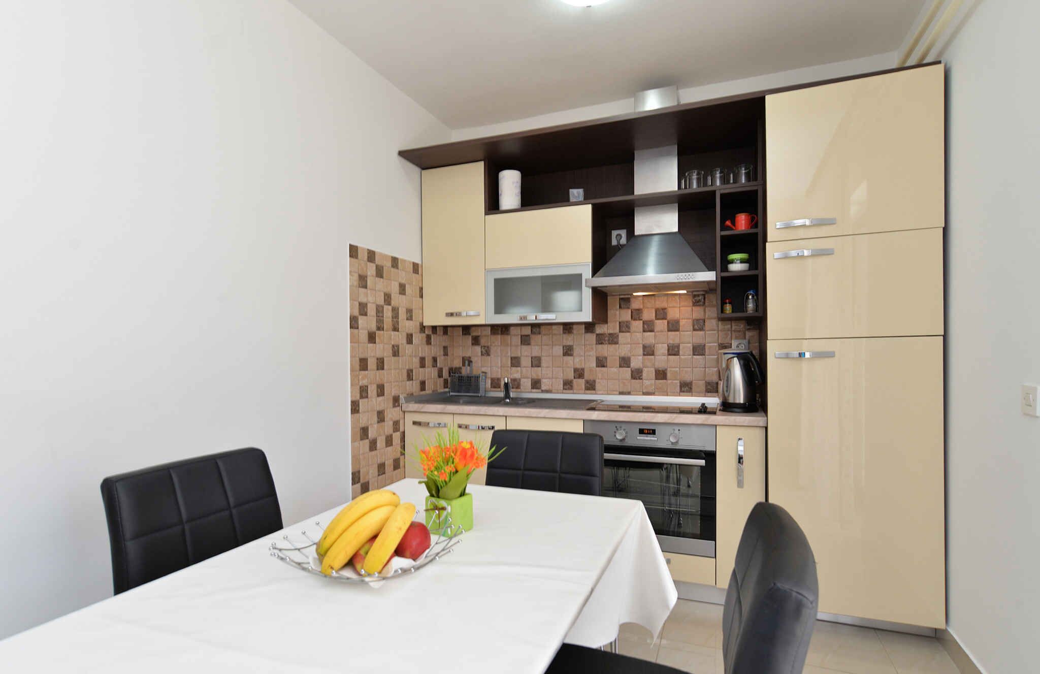 A compact kitchen with a microwave, stove, and cabinets. There is a dining table with chairs and a fruit basket.