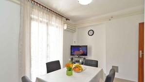 A dining area with a table set for two, a television on the wall, and a clock.