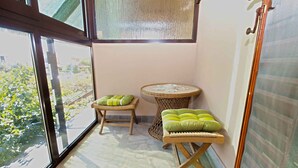 A balcony with a view of greenery, a wicker table with a cushion, and a small stool. - Holiday apartment with air conditioning and a view of the sea (Štinjan)