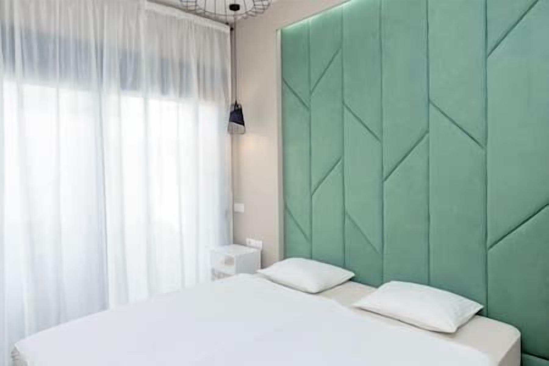 A modern bedroom with a green headboard, white bedding, and a bedside table with a lamp.