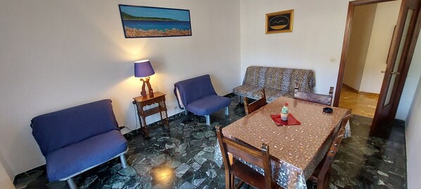 Une pièce avec un canapé bleu, un canapé à motifs, une petite table avec une serviette rouge, une lampe et un tableau au mur.