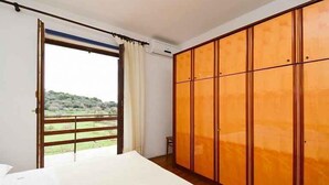 Una camera da letto con un armadio grande, un letto e un balcone con vista sul verde.