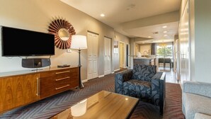 A hotel room with a flat-screen TV, a wooden cabinet, a patterned sofa, and a dining area in the background. - Indio CA | Desert Friends Trip | Pool & Lazy River | 3BR Sleeps 8 (Indio)