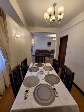 Un espace repas avec une longue table dressée pour six personnes, entourée de chaises en bois.
