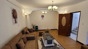 A living room with a sectional sofa, a coffee table, and a chandelier. - Highly rated, clean, and spacious guest house in the Bethel area! Great discount (Kolfe Keranio)