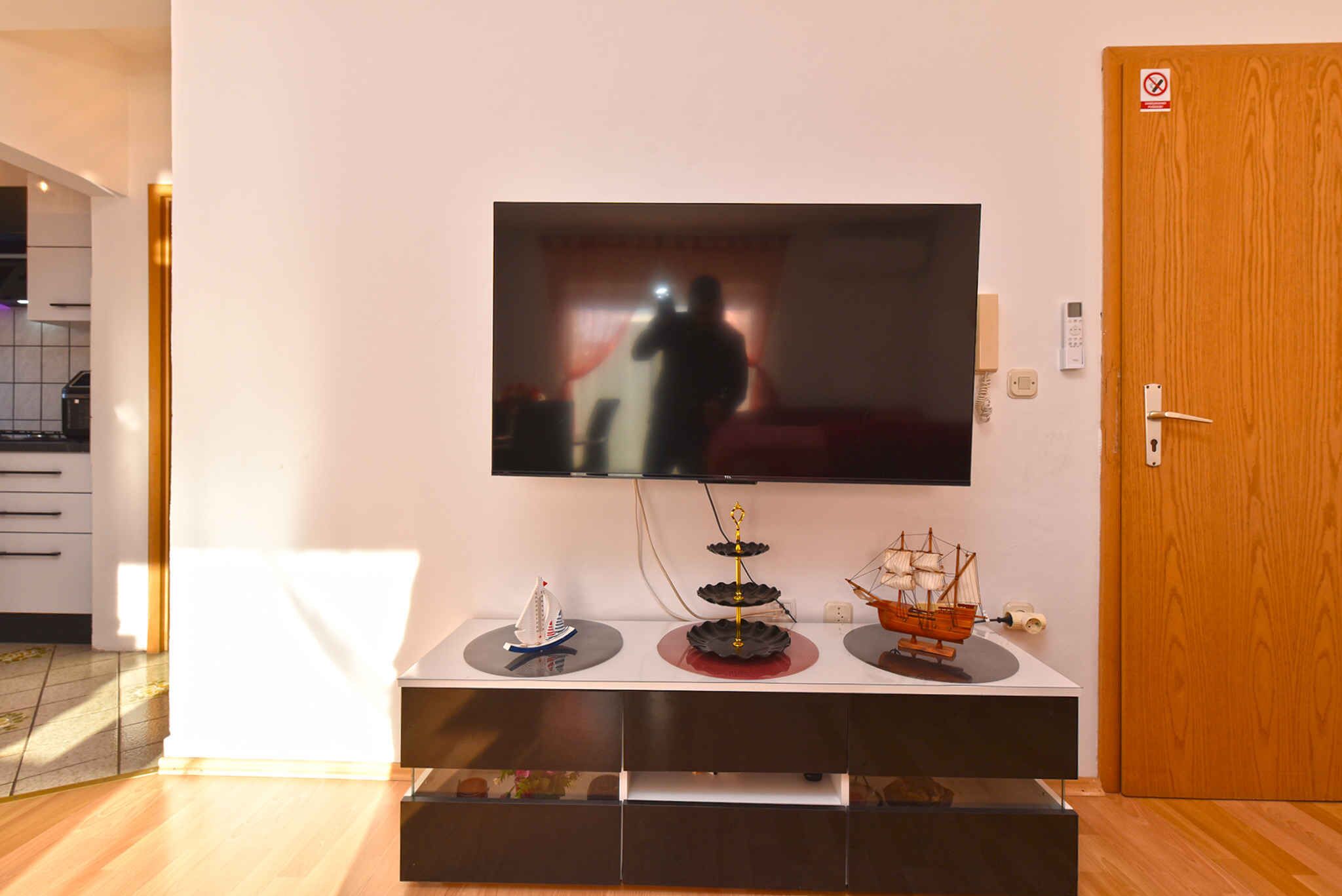 Ein modernes Wohnzimmer mit einem Flachbildfernseher an einer weißen Wand, einer Holztür und einem kleinen Tisch mit Modellschiffen.