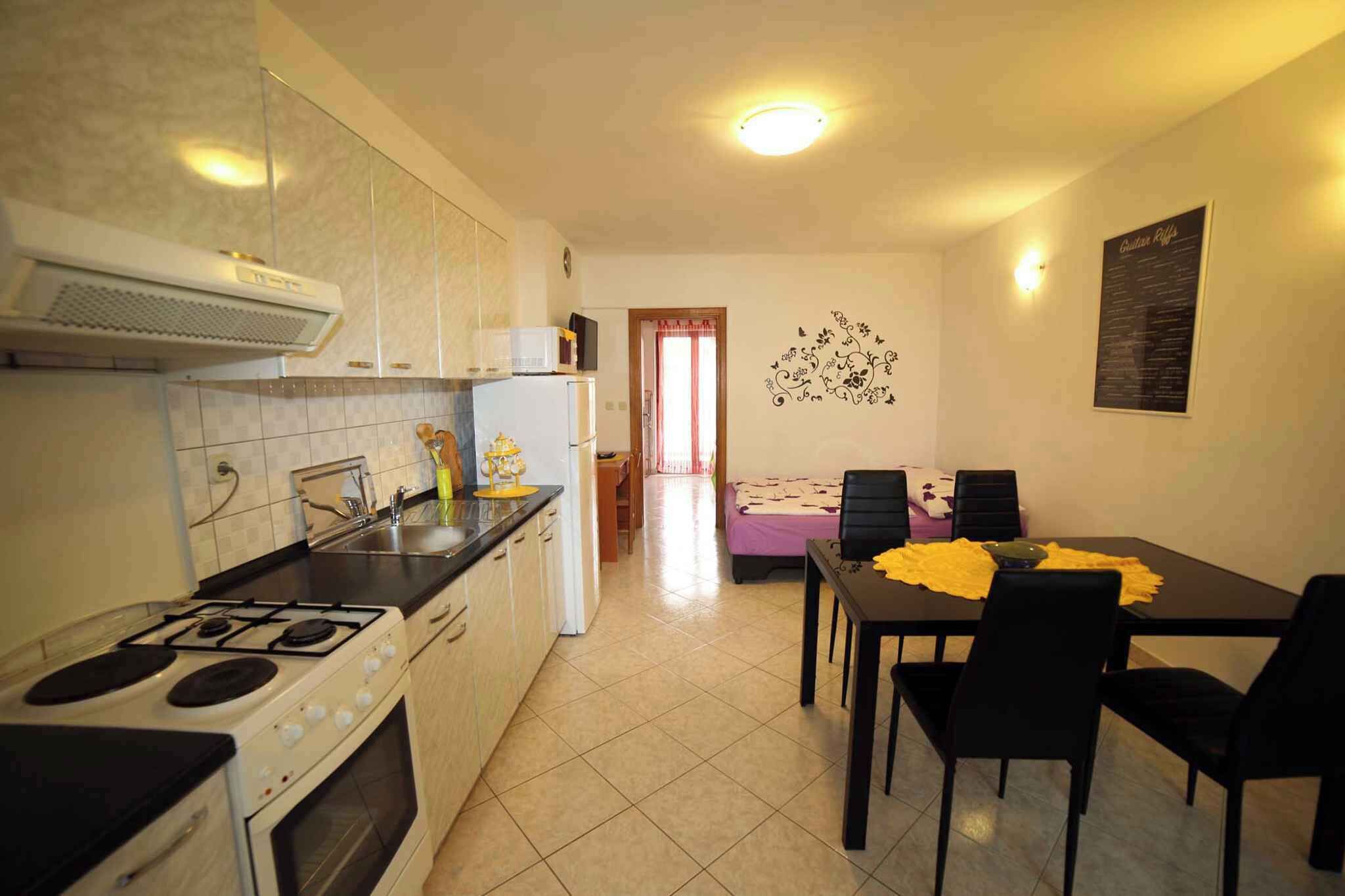 A compact kitchen with a stove, sink, and microwave. There is a dining area with a table and chairs.