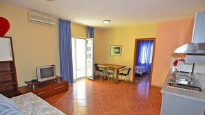 Habitación de hotel pequeña con cama, televisor, mesa de comedor con sillas, kitchenette y balcón con vistas.