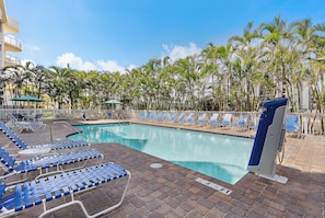 A pool area with lounge chairs and umbrellas, surrounded by palm trees.