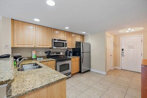 Una cocina con armarios de madera, electrodomésticos de acero inoxidable, encimeras de granito y suelo de baldosas.