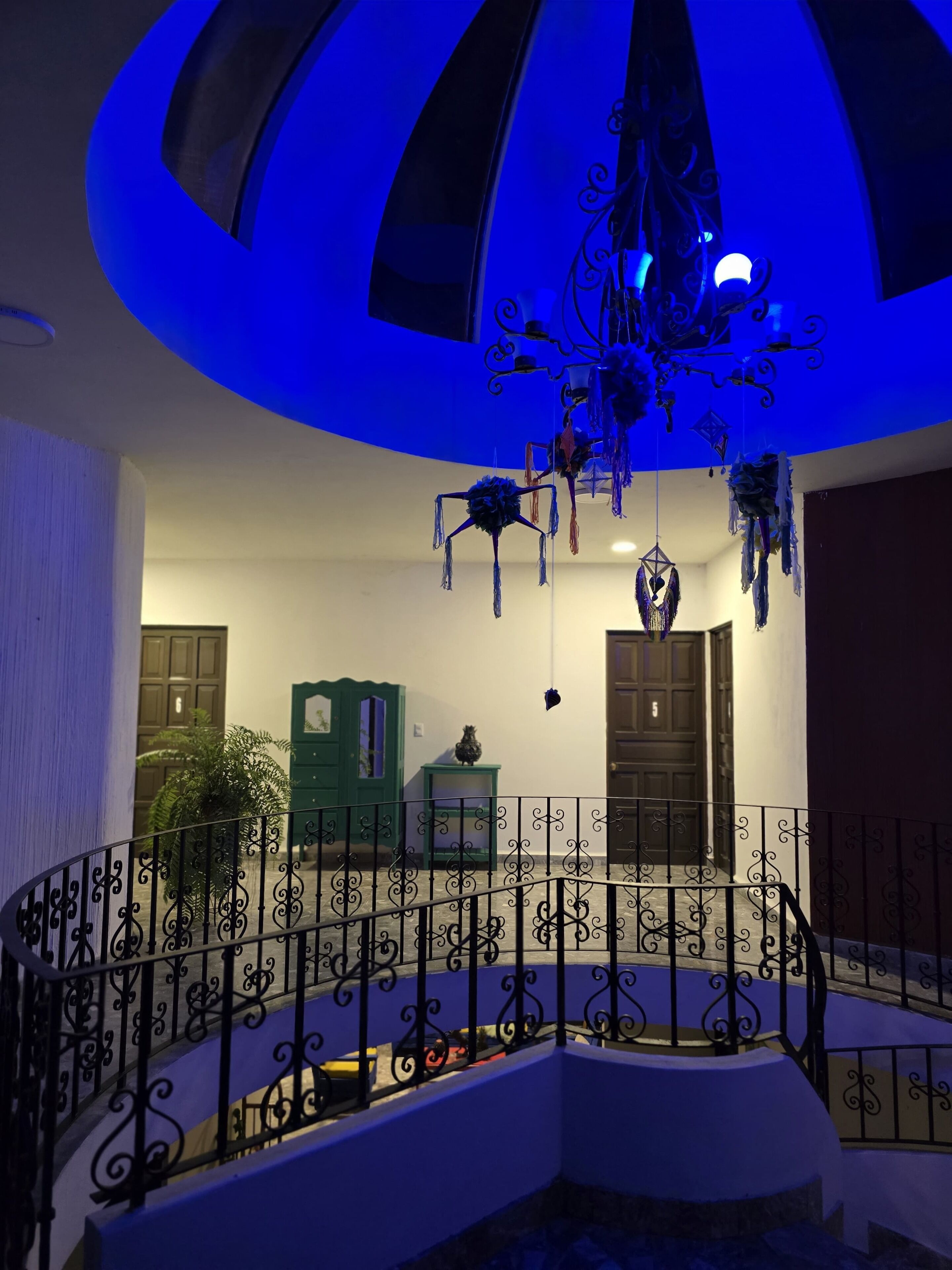 Eine Treppe mit aufwendiger schwarzer Geländer, einer blau beleuchteten Decke und einem grünen Schrank im Hintergrund.