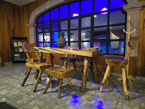 Una mesa de comedor de madera con sillas, un florero y una ventana con luz azul.