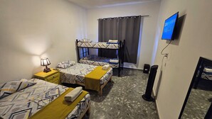 Una habitación de hotel con literas, televisor, escritorio con lámpara y espejo.